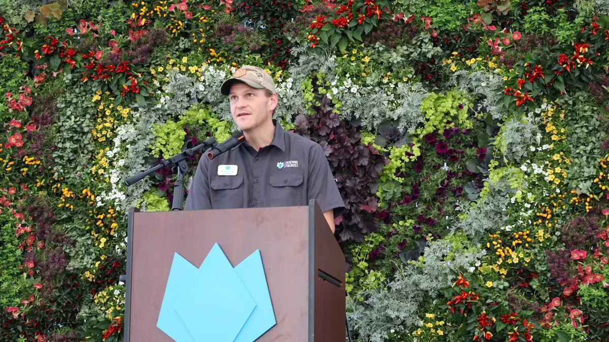 Ken Cox speaking at the PF podium in front of a living wall of flowers