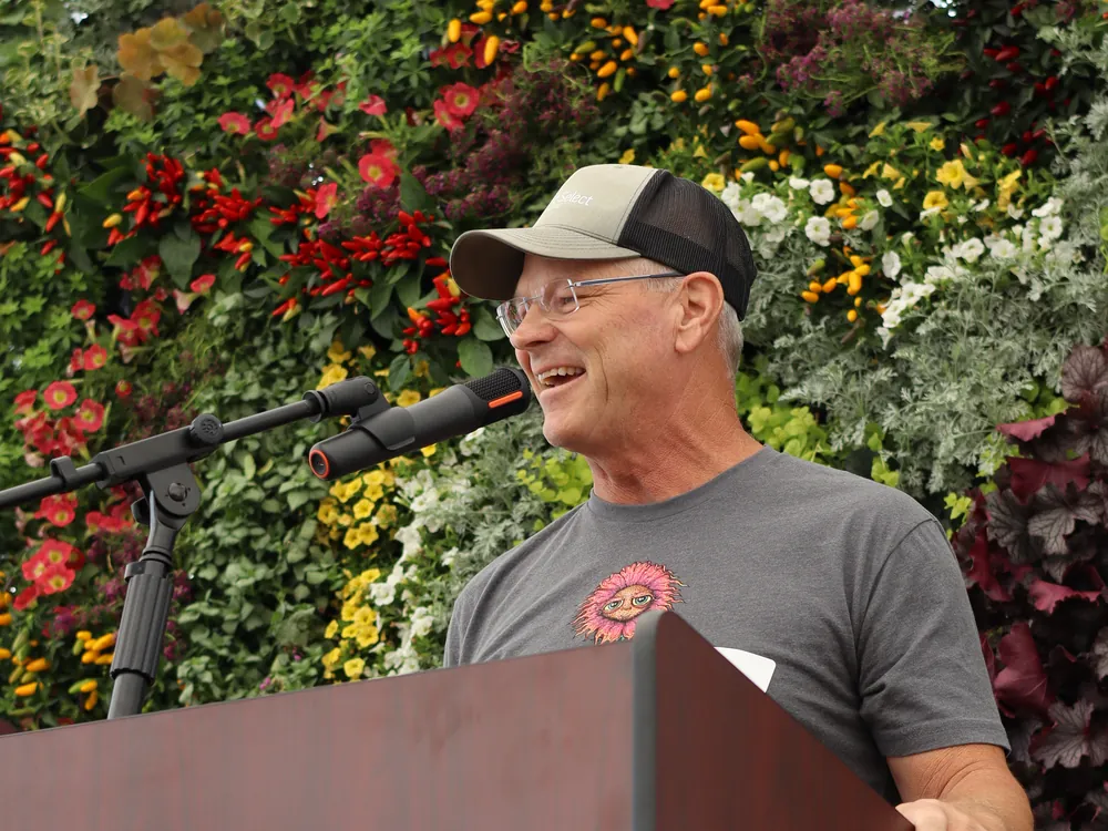 Ross Shrigley speaking at the podium in front of a living flower wall