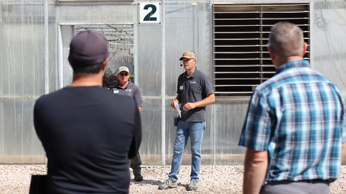 Cort Cox, in a headset mic, speaking to guests outside greenhouse 2 with Ethan behind him
